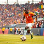 A dynamic scene of an Ivory Coast football player in action, wearing an orange and green jersey, dribbling a ball on a vibrant pitch, with the stadium packed with enthusiastic fans in the background waving flags and banners,